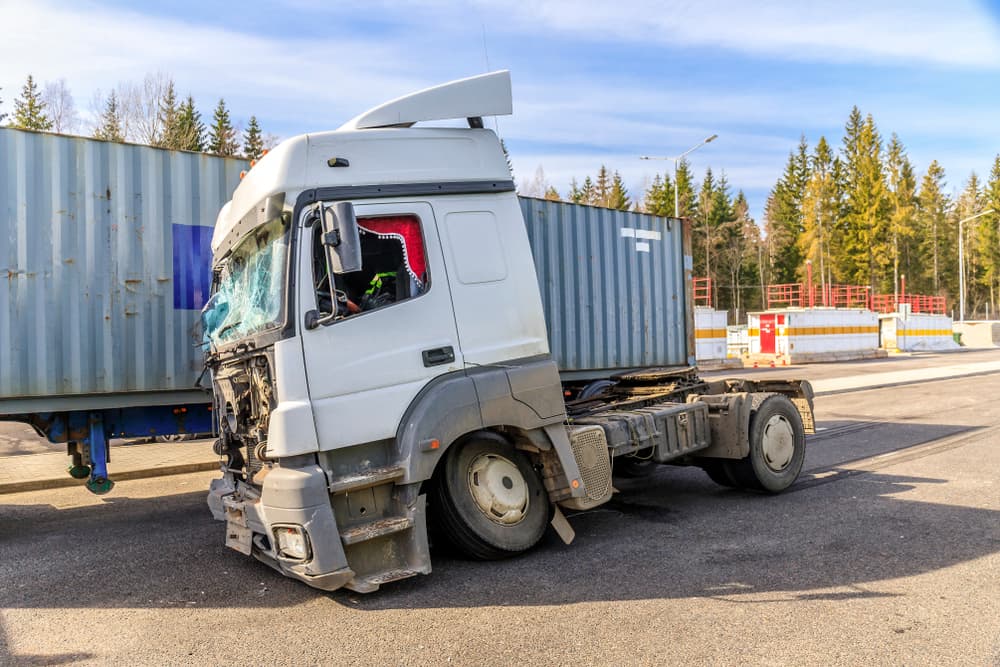 Jackknife truck accident showing a damaged semi-truck cab wedged against a shipping container at an industrial site after a collision.