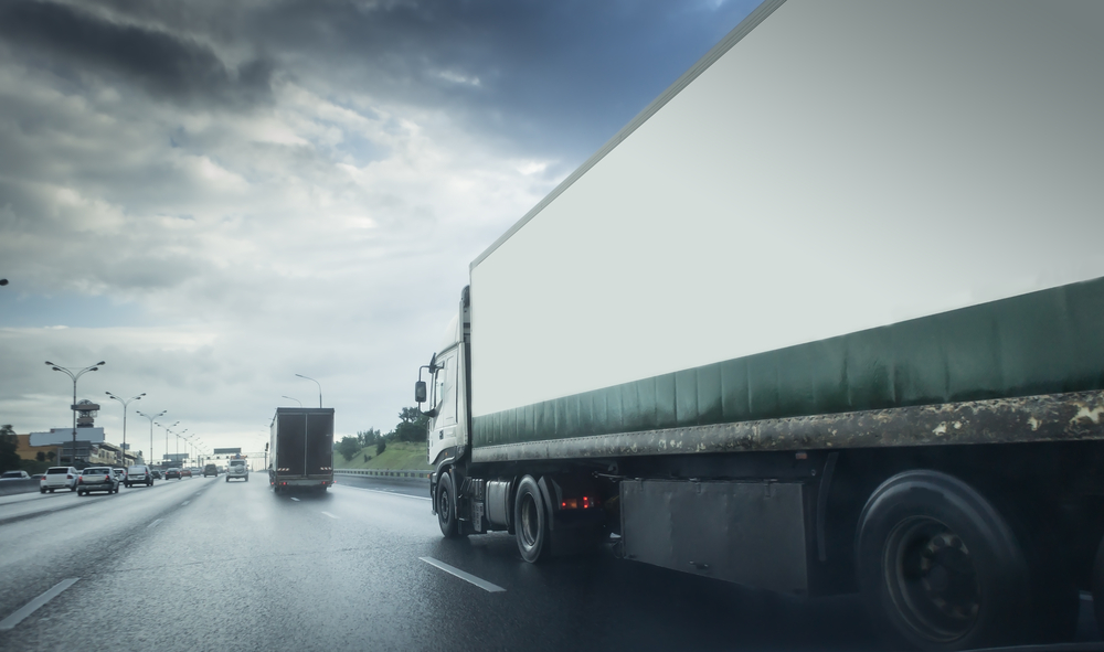 Truck in rain on asphalt wet road. Clouds and sun